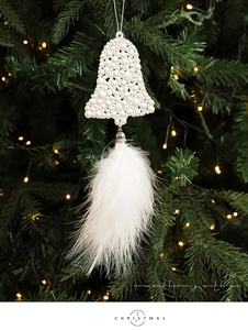 Close-up of a white pearl bell Christmas ornament with soft feathers on a lit tree