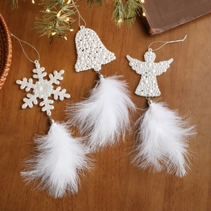 White feather snowflake bell and angel Christmas ornaments on a rustic wooden table