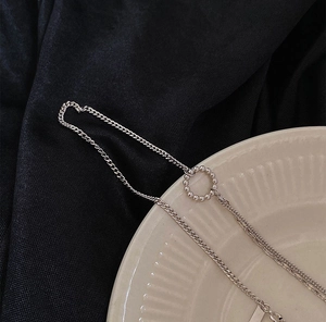 Macro detail of silver layered curb chain necklace featuring a minimalist bead circle pendant