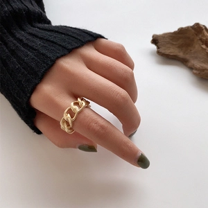 Detail of matte gold Cuban chain ring on finger with minimalist artistic background