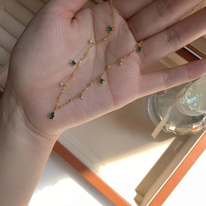 Detail of gold necklace with emerald drop pendant and square zircon accents on hand
