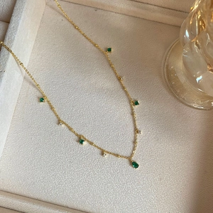 Close-up of gold chain necklace with emerald green stones in a beige jewelry box