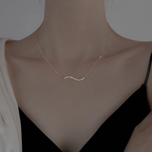 Elegant rose gold wavy pendant necklace with shimmering crystals on a woman's collarbone