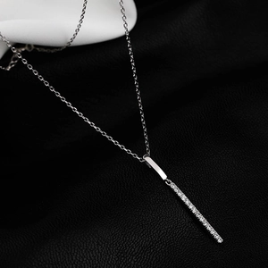 Macro detail of silver bar pendant necklace with sparkling zircon pavé on a silk background