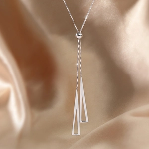Macro shot of geometric silver triangle pendant and adjustable box chain on satin