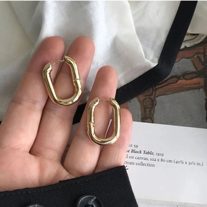 Minimalist gold U-shaped oval hoop earrings held in hand for size and style display