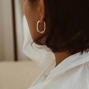 Detail of gold U-shaped oval hoop earring with textured hammered finish on female model