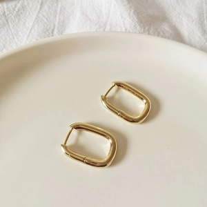Detailed close-up of golden U-shaped geometric earrings on a white ceramic plate