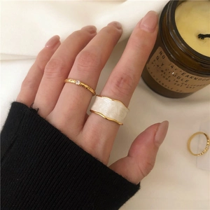 Close-up of gold-edged white enamel wave ring and slim zircon ring on hand