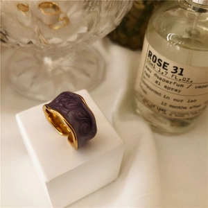 Detail of adjustable gold ring with purple marbled enamel and wave edges on white stand
