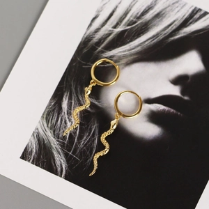 Detailed view of gold snake-shaped drop earrings with textured scales on a fashion card