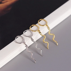 Macro shot of gold and silver snake earrings with detailed scale textures on white steps