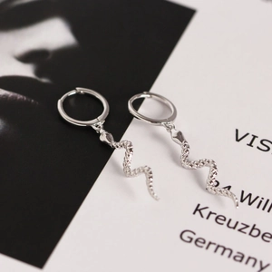 Macro shot of silver snake drop earrings with textured scales on an artistic magazine