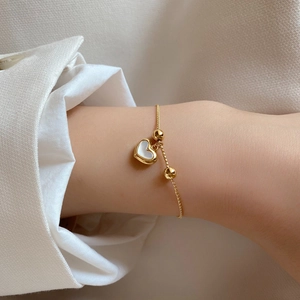 Gros plan d'un bracelet doré avec breloque cœur en nacre blanche sur un poignet