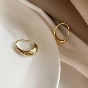 Close-up of polished gold crescent earrings placed on silk fabric and ceramic plate