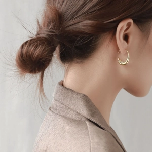 Close-up of polished gold C-shape drop earrings worn to show elegant profile and size