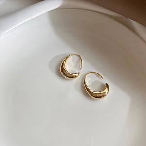 Detail of elegant gold drop earrings with polished finish on a white ceramic plate