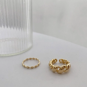 Détail de bagues en or torsadées et perlées sur un fond blanc minimaliste chic
