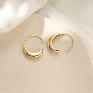 Macro shot of polished gold crescent hoop earrings on elegant silk fabric background