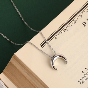 Détail du collier croissant de lune argenté sur page de livre au style minimaliste chic