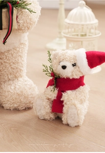 Close-up of cream teddy bear with red Christmas hat, scarf and festive pine decorations