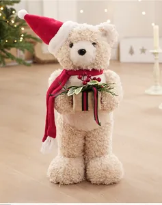 Close-up of cream teddy bear plush holding a gift box in a warm Christmas setting