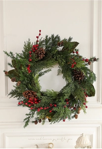 Nahaufnahme eines Weihnachtskranzes mit Zedernzweigen, roten Beeren und Zapfen an der Wand