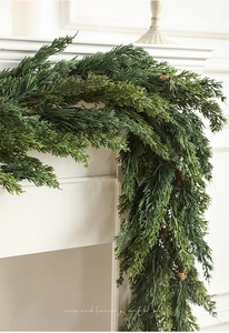 Detail of lush green artificial pine garland hanging on a modern white fireplace mantel