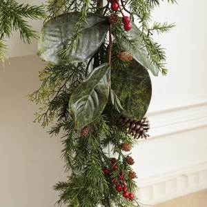 Weihnachtskranz mit Kiefernnadeln, Zapfen und roten Beeren an einer weißen Wand
