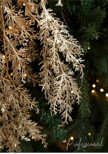 Gros plan d'une branche de paillettes dorées devant un sapin de Noël aux lumières chaudes