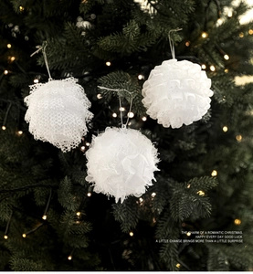 Detailed view of white textured foam Christmas balls with lace and tassel hanging on a tree