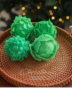 Detail of four green petal-shaped glitter Christmas balls on a woven tray with bokeh lights