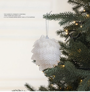Close-up of a white lace pinecone Christmas ornament on a lighted tree branch