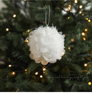Detailed view of white foam Christmas ball with petal texture on a lit festive tree