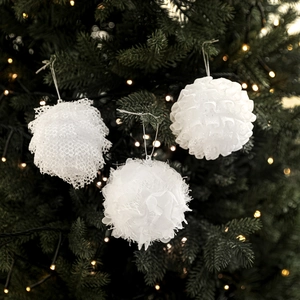 Three white foam Christmas balls with fabric and feather textures on a festive tree branch