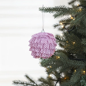 Pink lace foam Christmas ball ornament hanging on a tree with warm holiday lights