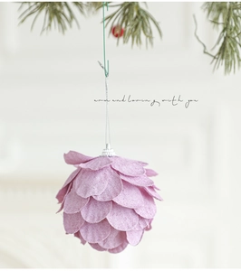 Bola de Navidad rosa con forma de pétalos y textura suave colgada en ramas de pino
