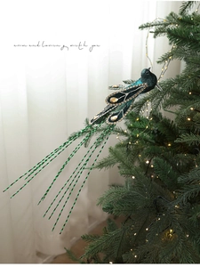 Detail of teal peacock Christmas ornament with faux gems on a lit holiday tree branch