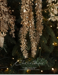 Detailaufnahme eines champagnergoldenen Glitzerzweigs an einem leuchtenden Weihnachtsbaum
