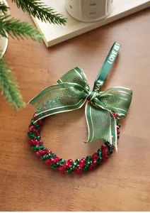 Close-up of red and green beaded Christmas wreath ornament with festive ribbon on wood
