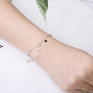Detailed view of silver star and moon charm bracelet on wrist with green leaf accents