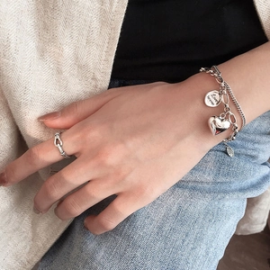 Detail of layered S925 silver bracelet featuring heart charm and Love Forever disc