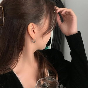 Close-up of a silver U-shaped chunky hoop earring worn by a model in a minimal setting