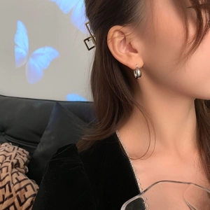 Close-up of minimalist silver teardrop earring worn on ear in a stylish indoor setting