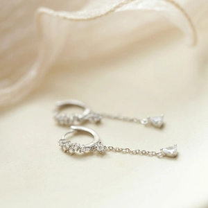 Detail of silver drop earrings featuring a long chain and triangle-cut zircon crystal