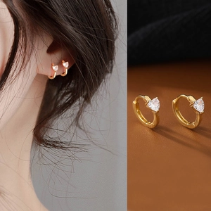 Detailed view of heart-shaped gold earrings with zircon on model and leather surface