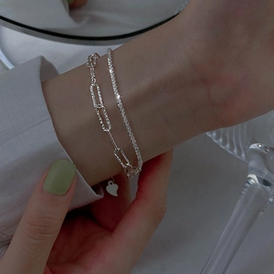 Detail of double-layer silver bracelet with paperclip chain and heart charm on wrist
