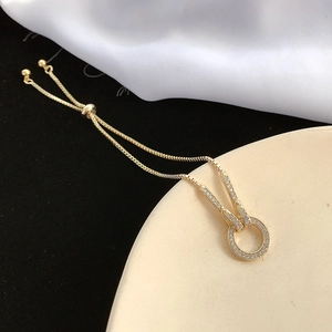 Dettaglio di un bracciale dorato regolabile con ciondolo in zircone su sfondo pregiato