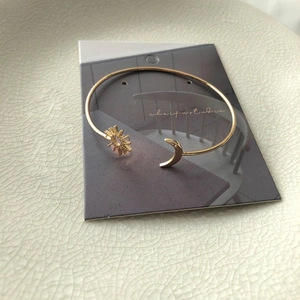 Detail of golden sun and moon open bangle bracelet resting on a stylish display card