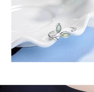Macro shot of silver open ring with dual green cat-eye leaves on a white ceramic plate